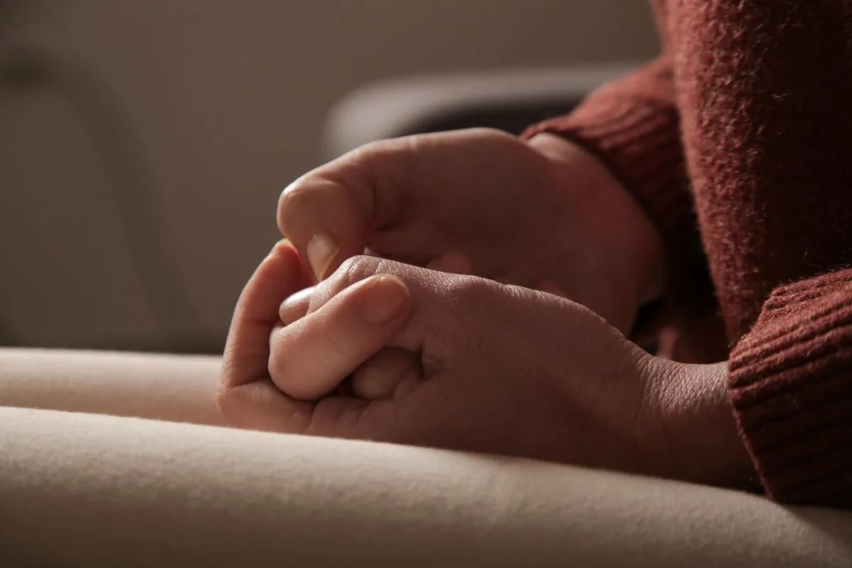 A person rests their clasped hands in their lap.