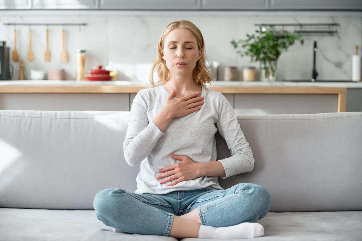 A woman rests one hand on her chest and the other on her abdomen while breathing.