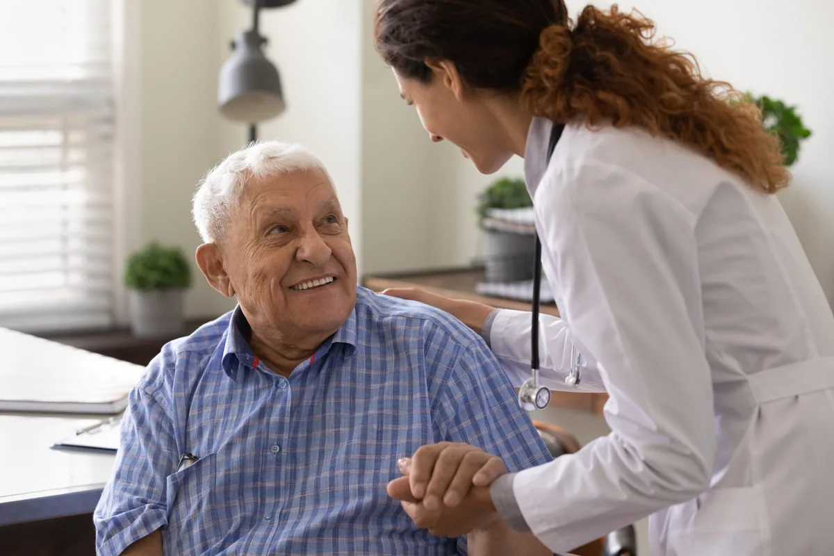 An older man smiles while speaking with a healthcare professional.