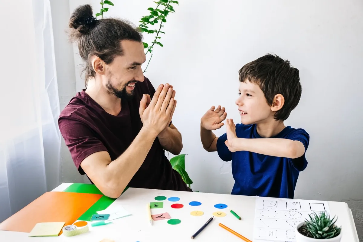 A parent and child practice hand movements together at a table.