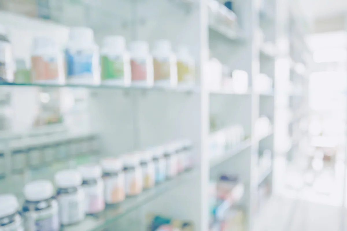 Shelves of medicines line a pharmacy aisle.