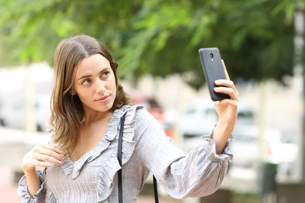 A woman holds up a phone outdoors.