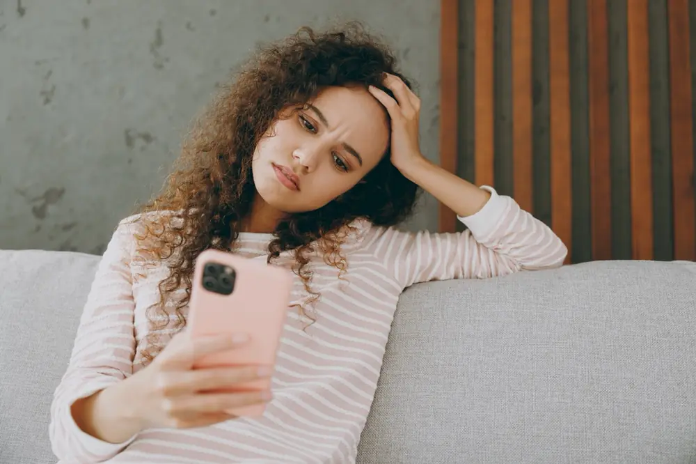 A woman pauses thoughtfully while looking at her phone.