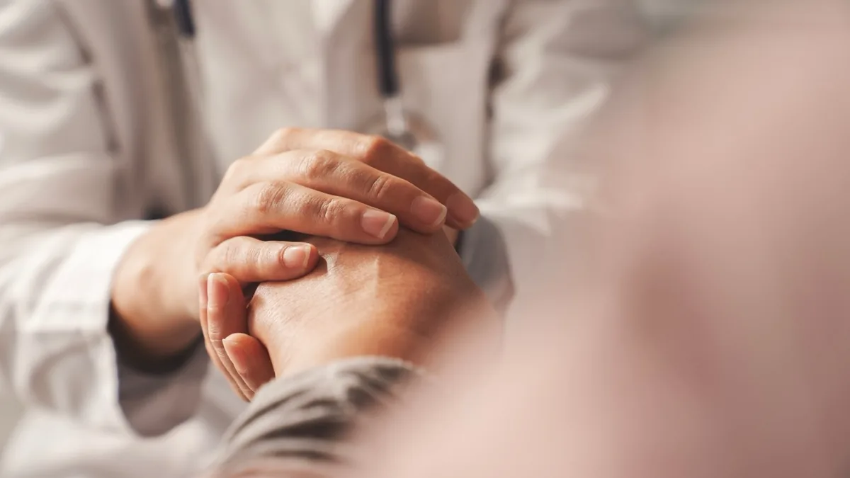 A healthcare professional holds a patient's hand during a conversation.
