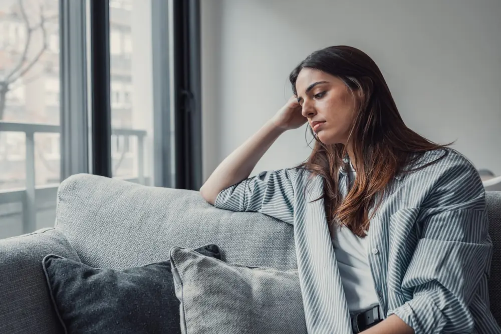 A woman sits on a sofa looking toward the window.