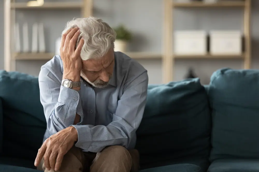 An older man sits with his head resting in one hand.